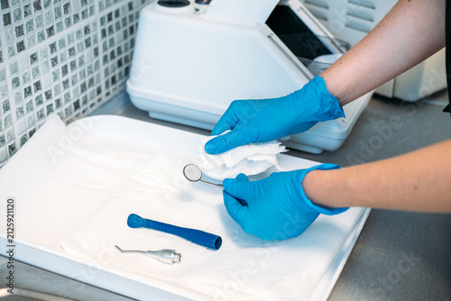 Cuadro en lienzo Gloved hands wipe small dental mirror with paper towel on tray before packaging