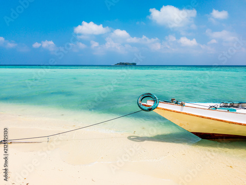 Traditional fishing boat resting on the sandy shore of Gleyang Island. Surrounded by clear turquoise water and a distant tropical island under a bright blue sky
