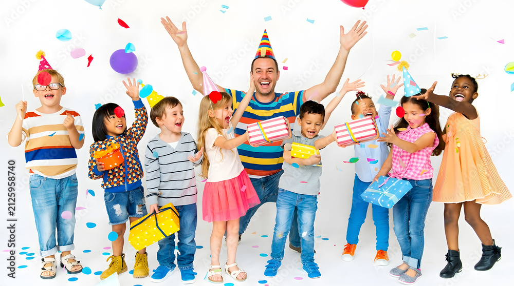 Naklejka premium Group of cheerful multiethnic children celebrating birthday party with dad holding gifts and raising hands under falling confetti against white studio background