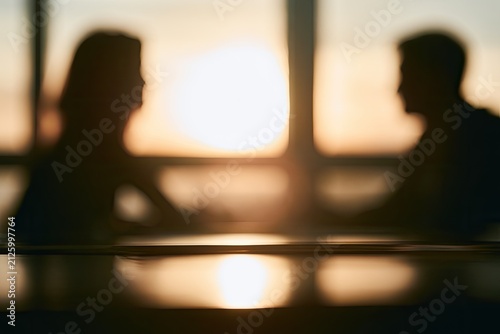 Silhouettes of two people facing each other across a table, bathed in warm sunset light