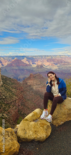 A gorgeous young Woman sits on a rock facing the American Grand Canyon National Park in Arizona, Usa.