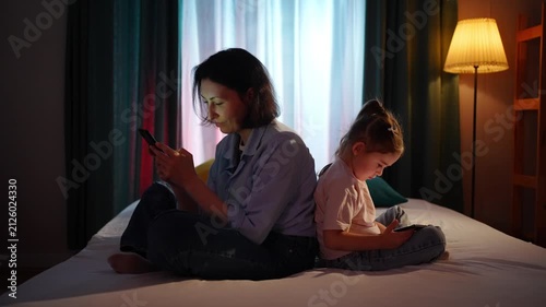 Mother and young daughter sitting together but ignoring each other while using smartphones