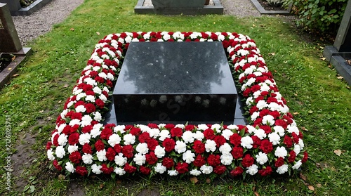 A grave decorated with red and white flowers in a cemetery.