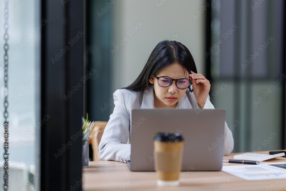 Obraz premium Businesswoman experiencing headache and frustration while working on laptop, facing stress and burnout at office desk