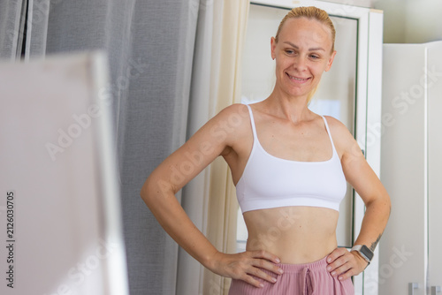 Confident woman smiling, standing in front of mirror, appreciating her progress journey with weight loss, health, wellbeing, and positive body image