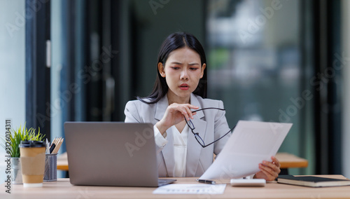 Canvas Print Stressed asian businesswoman experiencing fatigue and pressure, reading document