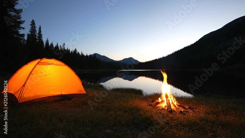 Camping near lake at sunset with bonfire glow.