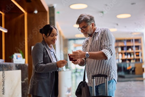 Happy female concierge assisting guest with checking in at hotel.