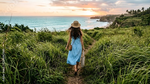 Woman in blue dress walking towards the ocean at sunset.