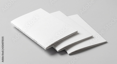 Three blank white saddle-stitched booklets stacked diagonally on a light gray background in a high-angle studio scene.