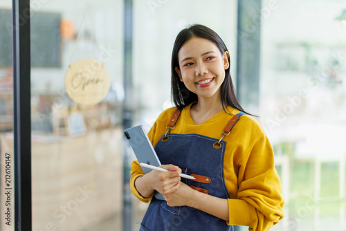 Foto Woman small business owner in apron smiling holding tablet and stylus at coffee