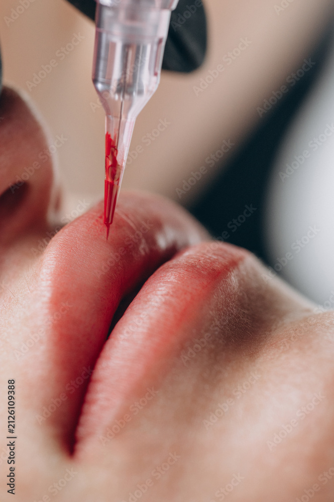 Fototapeta premium Extreme close up of a permanent makeup artist performing a lip blush tattoo procedure with a PMU machine in a professional beauty salon.