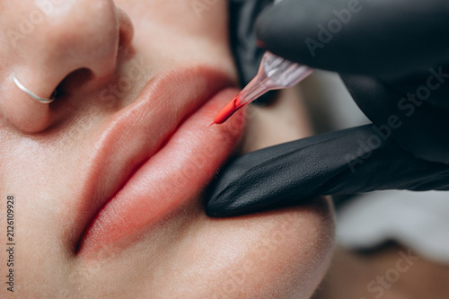 Fotografie Macro close up of a permanent makeup artist performing a lip blush tattoo procedure with a PMU machine in a professional beauty salon