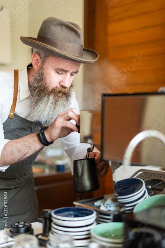 Obraz na plátně Bearded man in hat making coffee at a cafe with focused expression