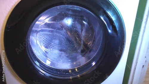 Washing machine drum spinning with blue-tinted water during washing cycle in home laundry.