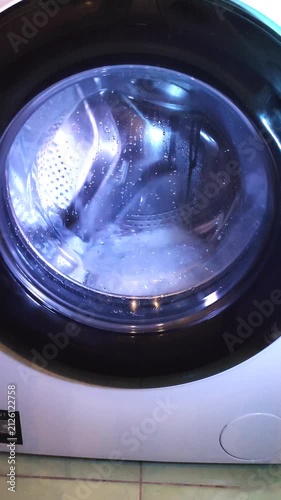 Washing machine drum spinning with blue-tinted water during washing cycle in home laundry.
