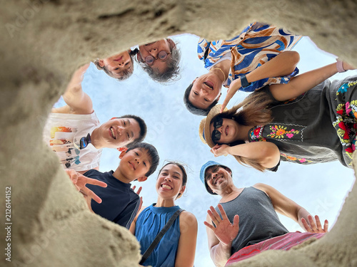 Asian multi generation family taking bottom up hole beach selfie on summer vacation, multi-generational Thai family with gen alpha kids smiling looking down at camera, happy creative holiday portrait.