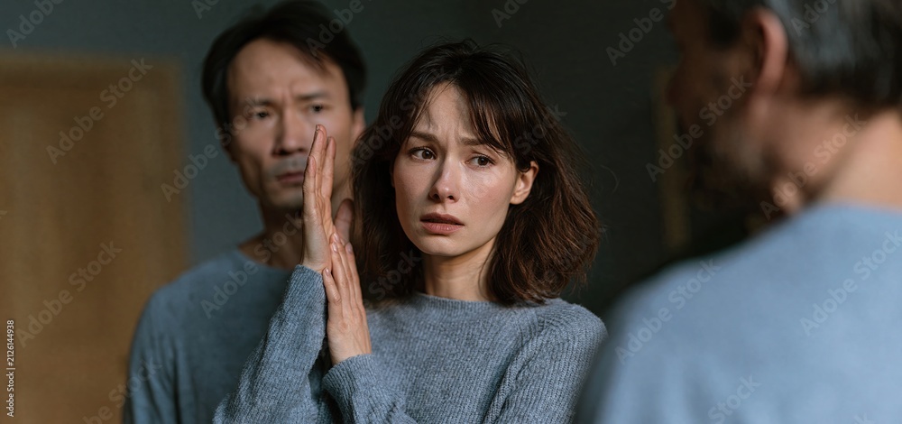 Fototapeta premium A frightened woman protects herself from an angry partner in a dimly lit room, highlighting domestic violence awareness.