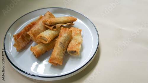 Fotografía A white plate filled with fried spring rolls containing sweet purple yam and chocolate, placed with generous negative space on the side