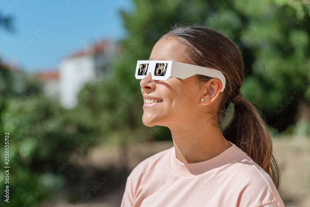 Obraz premium Smiling young woman wearing protective paper glasses to safely watch solar eclipse.