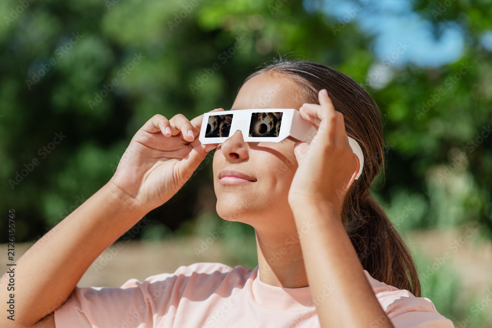Obraz premium Smiling young woman wearing protective paper glasses to safely watch solar eclipse.