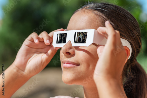 Fotografie Smiling young woman wearing protective paper glasses to safely watch solar eclipse