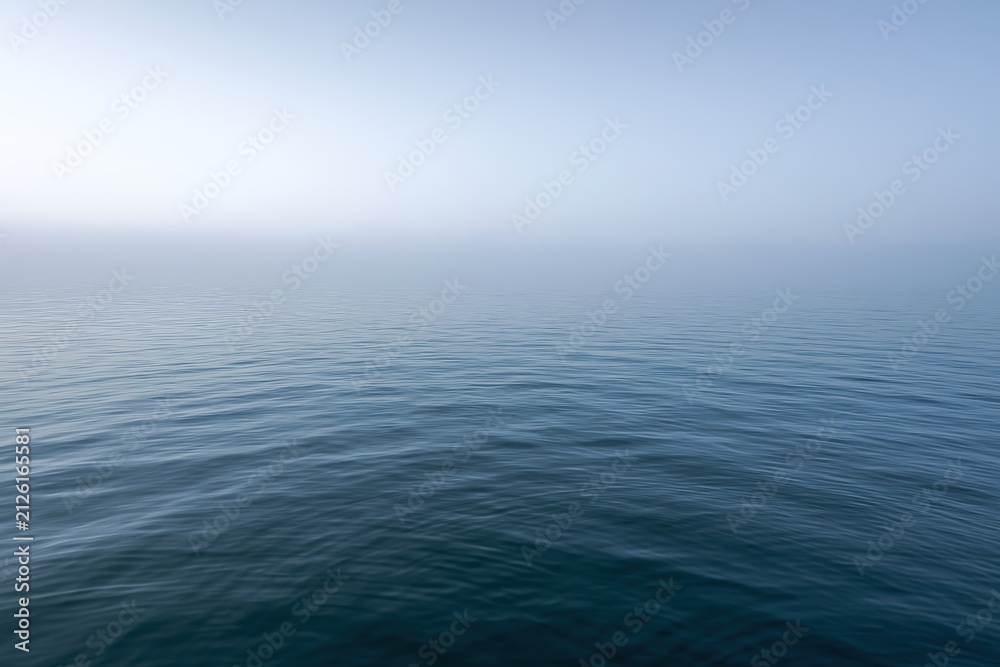 Obraz premium Glassy blue sea under a foggy horizon in tranquil seascape