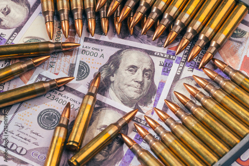 bullets over one hundred US dollar bills banknotes as a conceptual metaphor for global geopolitical conflict war finance military capitalism arms trade and budget defense with copy space.
