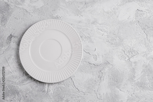 Empty white ceramic plate on a light gray decorative plaster background with copy space. Minimal table setting for food presentation, menu design, recipes, restaurant branding and culinary mockups.