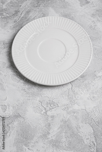 Empty white ceramic plate on a light gray decorative plaster background with copy space. Minimal table setting for food presentation, menu design, recipes, restaurant branding and culinary mockups.