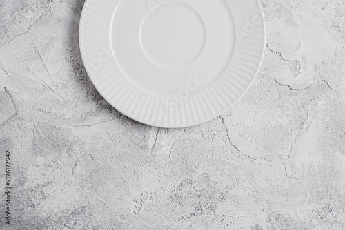 Empty white ceramic plate on a light gray decorative plaster background with copy space. Minimal table setting for food presentation, menu design, recipes, restaurant branding and culinary mockups.