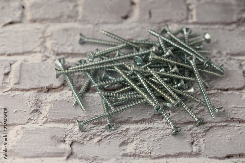 Принти на полотні A group of metallic screws is scattered on a light gray brick surface, their gleaming heads catching the light