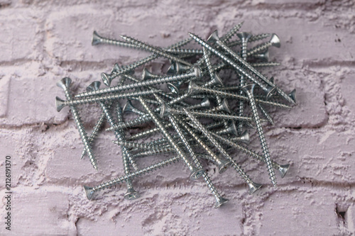 Bild auf Leinwand A multitude of gleaming metal screws lies haphazardly on a rustic brick surface, reflecting light from nearby tools