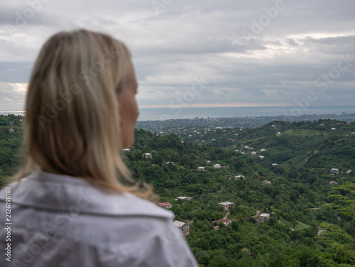 Foto Blonde woman standing with her back to the camera, looking out at the lush green