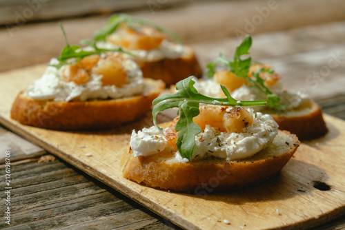Fotografía Bruschetta or crostini with cream cheese, shrimp and arugula on wooden board