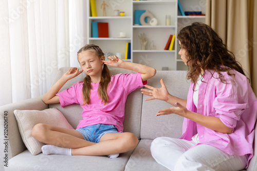 фотографія Young daughter closing her eyes and covering her ears while mother speaking and