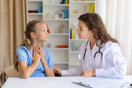 Konstfotografi Female doctor listening attentively as young girl touches her throat and describ
