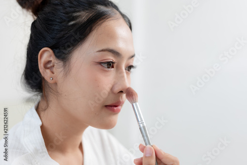 Obraz na płótnie Calm beautiful young asian woman applying makeup to her face using cosmetic brus