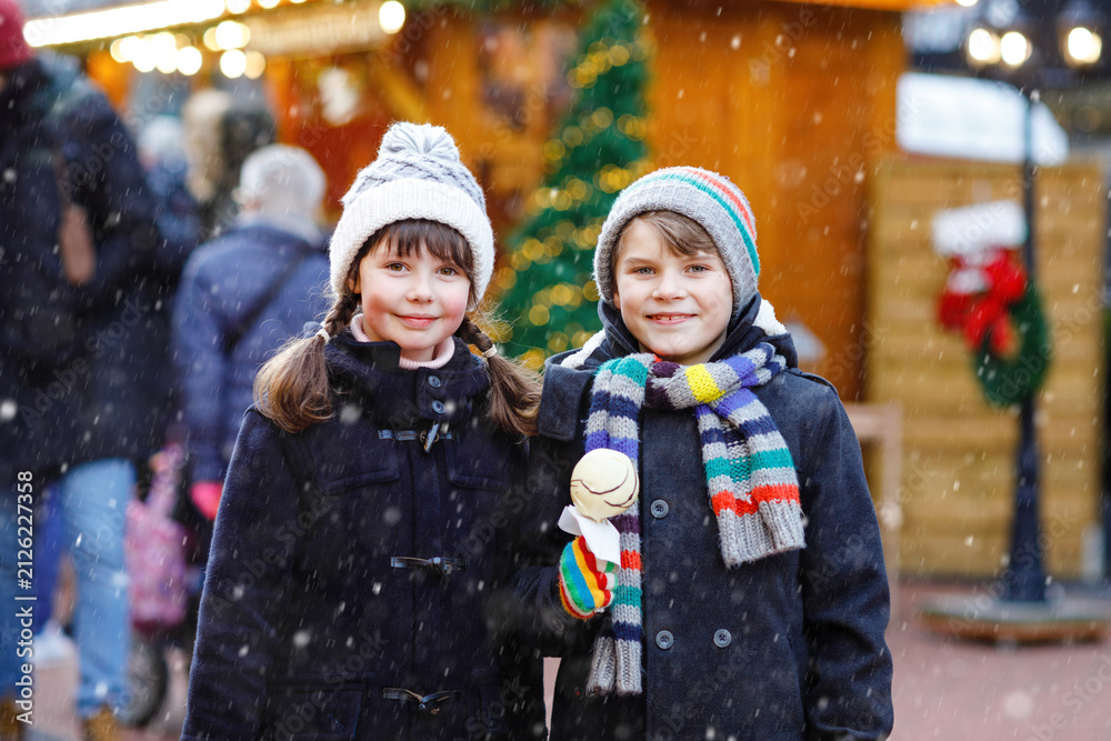 Obraz premium Little cute kid girl and boy eating white chocolate-covered strawberries and apple skewers at German Christmas market. Happy siblings. Real life, real people, snowy festive joy