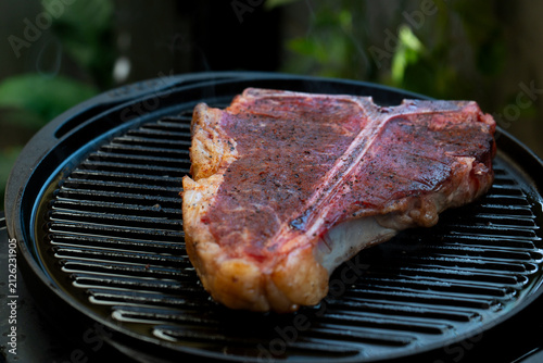 Man grilling a porterhouse steak over cast iron griddle, the smoke is visible through the high-heat sear, suitable for summer grill theme	