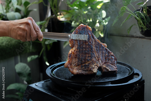 Man grilling a porterhouse steak over cast iron griddle, the smoke is visible through the high-heat sear, suitable for summer grill theme	