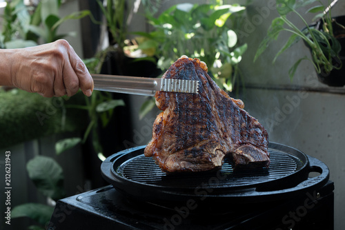 Man grilling a porterhouse steak over cast iron griddle, the smoke is visible through the high-heat sear, suitable for summer grill theme	