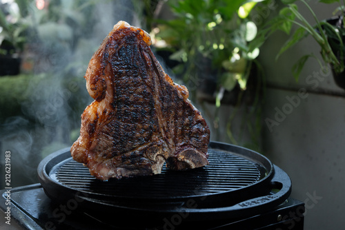 Man grilling a porterhouse steak over cast iron griddle, the smoke is visible through the high-heat sear, suitable for summer grill theme	