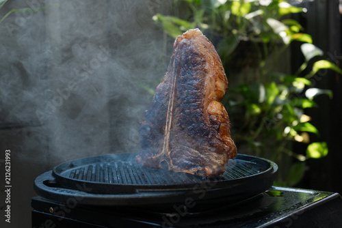 Man grilling a porterhouse steak over cast iron griddle, the smoke is visible through the high-heat sear, suitable for summer grill theme	