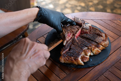 Man plating a medium rare porterhouse steak on a rustic black stone plate, perfect for summer grilling theme