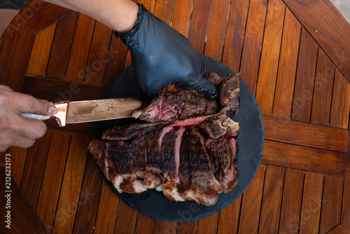 Man plating a medium rare porterhouse steak on a rustic black stone plate, perfect for summer grilling theme