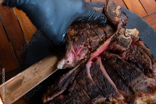Man plating a medium rare porterhouse steak on a rustic black stone plate, perfect for summer grilling theme