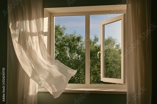 Open white casement window with sheer curtains blowing in the breeze