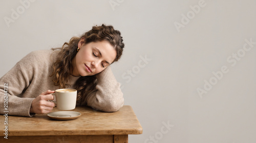 A woman in a beige sweater resting her head on her hand while holding a warm cup of coffee ad social media download thambnail poster web template event festival 2026 2027 2028