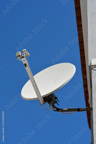 Quadro su tela A low angle shot of a white parabolic satellite dish receiver mounted on a white building wall under a clear blue sky